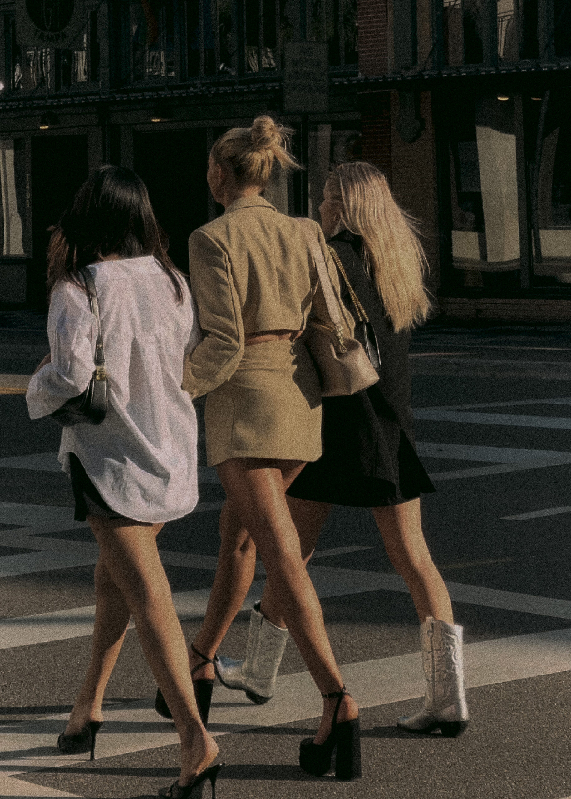 Building trust as an influencer lifestyle image of three women walking across a city street in chic outfits, featuring a neutral blazer set, oversized white shirt, and black dress styled with heels and boots, capturing effortless, real-life fashion inspiration